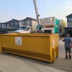 Large yellow dumpster with You Junk It logo in front of a construction site, ready for debris removal.
