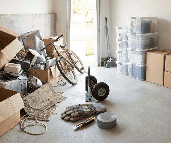 A cluttered storage space filled with open boxes, electronic devices, a bicycle, and various tools, indicating a recent move or storage organization.